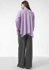 Lichtpaarse shirt met een langere achterzoom, gecombineerd met wijde grijze broek met een gestructureerd patroon en subtiele accenten.