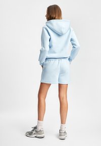 Lyseblå hettegenser med snor og kengurulomme, kombinert med matchende shorts. Myk stoff, avslappet passform, ingen synlige logoer, enkel design.