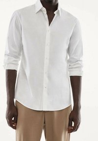 Weißes Langarmhemd aus glattem Stoff mit klassischem Kragen und durchgehender Knopfleiste. Taillierte Passform mit aufgekrempelten Manschetten.