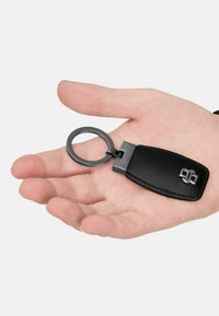 Black leather keychain with a smooth texture, featuring a silver metal ring and an attached rectangular tag with embossed logo detail.