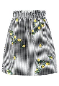 Schwarz-weißer Karorock mit smockiertem Bund, verziert mit gelben gestickten Blumen und grünen Stielen, die über den Stoff verteilt sind.