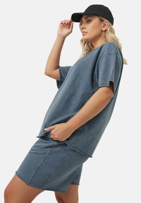 Niebieska bawełniana koszulka o oversize'owym kroju i krótkich rękawach, zestawiona z dopasowanym niebieskim szortami-dżinsami. Uzupełniona czarną czapką.