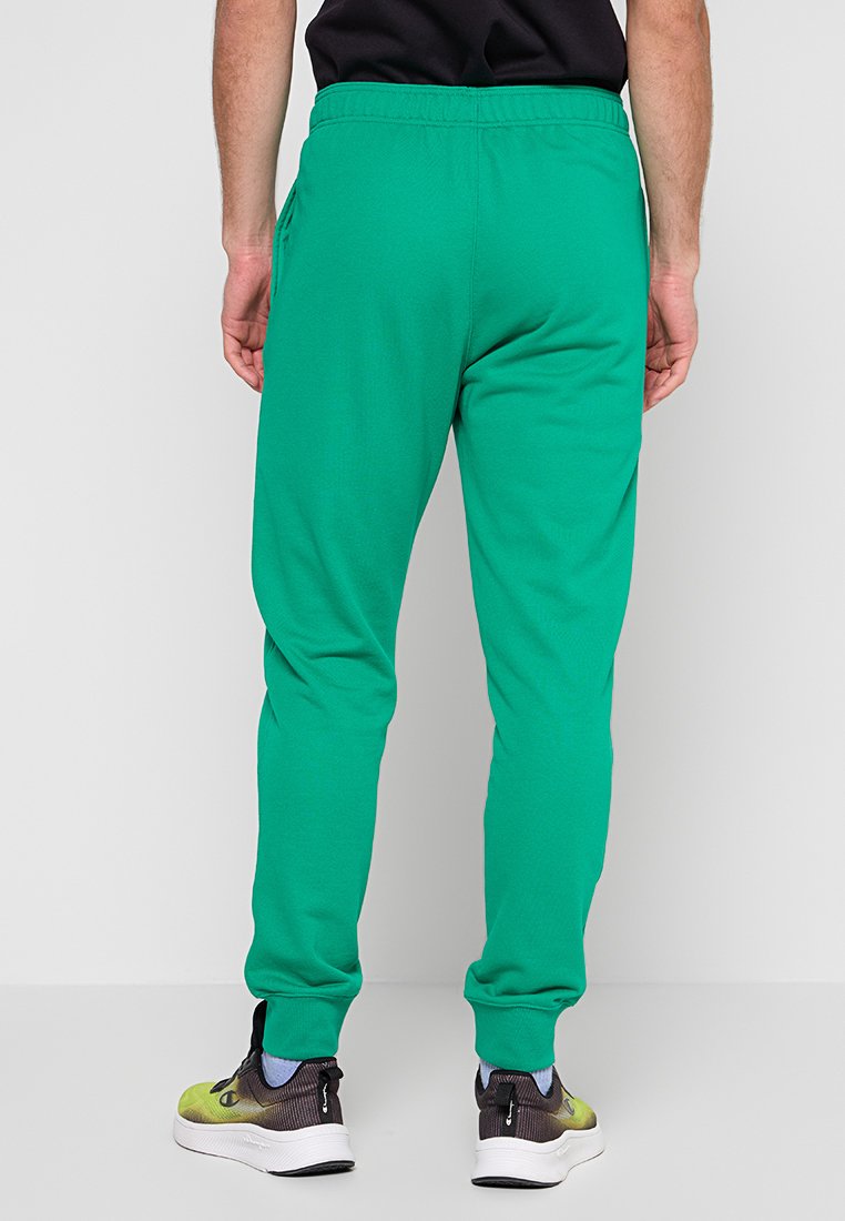 Joggers verdes de algodón con un corte relajado, cinturilla elástica, bolsillos laterales y puños ajustados, combinados con zapatillas negras y amarillas.