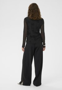 Melnas garas piedurknes tops ar strukturētu ziedu rakstu, kombinēts ar platām melnām biksēm ar sānu šķēlumiem un norādītām dzīvokļa apaviem.