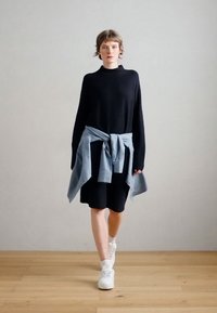 Černý pletený top s dlouhým rukávem, volnější střih, doplněný světle modrým svetrkem zauzlovaným v pase a černou sukní ke kolenům. Bílé tenisky.