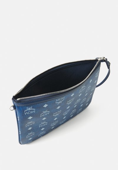 Pungă de piele albastră cu fermoar, cu un model repetitiv al logo-ului alb MCM, dotată cu o brăţară, pe un fundal alb.