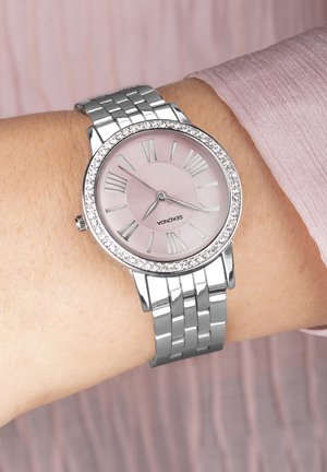 Montre-bracelet en argent avec un cadran rose pâle, des chiffres romains et une lunette sertie de cristaux. Elle dispose d'un bracelet à maillons métalliques.