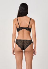 Set di lingerie in pizzo nero con design scallop. Spalline regolabili sul reggiseno con chiusura a gancio. Il tessuto presenta un motivo testurizzato.