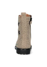 Beige enkellaars met geperforeerde textuur, zwarte steraccenten en een zwarte rubberen zool. Voorzien van een rits aan de zijkant voor gemakkelijke instap.