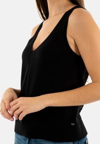 Débardeur en tricot noir avec un col en V, doté de bretelles larges, d'un ourlet côtelé et de détails de couture subtils à l'avant et sur les côtés.