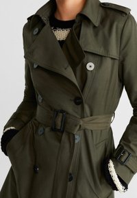 Olivgrüner Trenchcoat aus weichem Stoff, mit einem doppelreihigen Design, großen Knöpfen, einem taillierten Schnitt mit Gürtel und aufgesetzten Taschen.