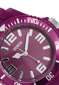 Montre violette avec un cadran mat, des aiguilles argentées et de grands chiffres blancs. Elle dispose d'une lunette unidirectionnelle et d'un bracelet en caoutchouc.