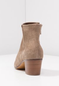 Brązowy zamszowy botek za kostkę z zaokrąglonym noskiem, tylnym zamkiem błyskawicznym i drewnianą, wygodną piętą. Wierzch buta ma gładką fakturę.