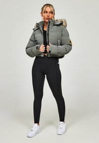 Afgestemde olijfgroene cropped puffer jacket met een faux fur gevoerde capuchon, een rits aan de voorkant en een logo patch. Draag het over zwarte leggings en witte sneakers.