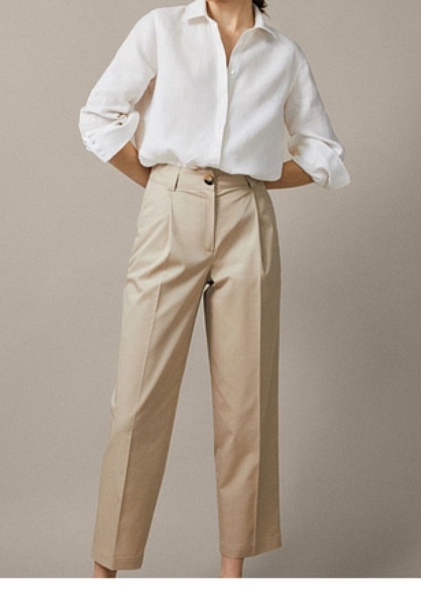Pantalons beiges ajustés à taille haute, avec des poches latérales et une fermeture à un bouton, associés à une chemise blanche à boutons.
