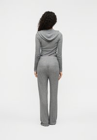 Γκρι ολόσωμη φόρμα με μακριά μανίκια και κουκούλα, κατασκευασμένη από απαλό ύφασμα. Διαθέτει εφαρμοστό μπούστο και φαρδιά πόδια με κυματιστά τελειώματα.