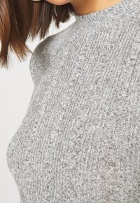 Maglione grigio a coste con design a collo alto. La texture è morbida con leggere variazioni di colore. Vista ravvicinata del tessuto.