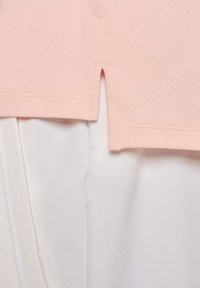Top de malla rosa claro con aberturas laterales, superpuesto sobre un fondo de tela blanca. Textura suave y diseño casual, estética minimalista.