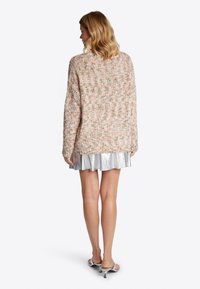 Hellrosa gestrickter Pullover mit bunten Einsprenkgungen, langen Ärmeln und lockerer Passform, kombiniert mit einem glänzenden silbernen Plissierrock.