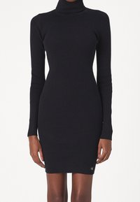 Robe col roulé noire côtelée à silhouette près du corps. Manches longues et logo discret à l'ourlet. Texture lisse et coupe ajustée.