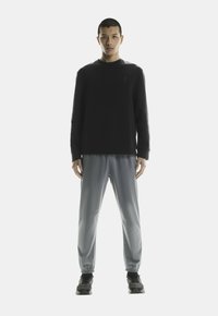 Zwarte sweatshirt met een ronde halslijn, grijze sportbroek met elastische boorden en zwarte sneakers. Eenvoudig ontwerp met minimale details.