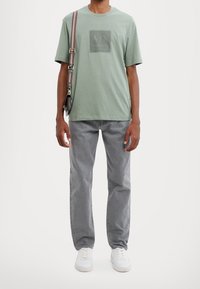 Mentolově zelené bavlněné tričko s potiskem loga, kombinované s světle šedými džíny a bílými teniskami. Obsahuje křížovou tašku se pruhovaným popruhem.
