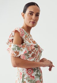 Robe florale avec des manches en volants, présentant une base blanche et des motifs botaniques roses, orange et verts. Texture de tissu léger.