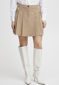 Beige plissert skjørt med knappelukking, kombinert med hvite støvler til kneet med teksturert overflate og spiss tå-design.