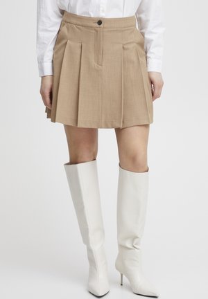 Gonna plissettata beige con chiusura a bottone, abbinata a stivali bianchi fino al ginocchio con superficie texturizzata e punta a forma appuntita.