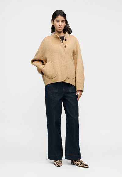 Μπεζ σακάκι από μείγμα μάλλινης ύφανσης με στρογγυλεμένο γιακά, τσέπες στο μπροστινό μέρος και τρία κουμπιά. Συνδυασμένο με σκούρα τζιν παντελόνια ευρέως ποδιού και παπούτσια με λεοπάρ μοτίβο.