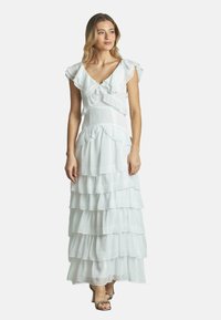 Weißes, geschichtetes Maxikleid mit Rüschenschläfen und tailliertem Oberteil. Hergestellt aus leichtem Stoff, mit sanften, fließenden Schichten.