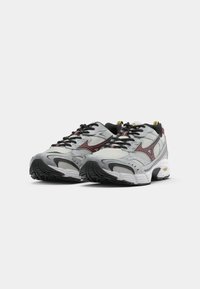 Gray athletic shoes with mesh upper, black laces, red accents, and a patterned rubber sole. Features cushioning and a padded collar.