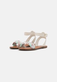 Tkané sandály s pastelovými materiály, splétaným předním páskem a nastavitelným páskům na kotníku se zlatou sponou. Plná hnědá podrážka.
