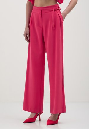 Pantaloni a gamba larga di un vivo colore rosa, realizzati in tessuto liscio e leggero. Presentano una cintura annodata in vita e tasche laterali.