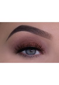 Close-up van een oog met gelaagde bruine en bronzen oogschaduw, gedefinieerde donkere wimpers en een netjes gevormde wenkbrauw, tegen een lichte huidskleur.