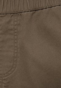 Gros plan d’un tissu marron avec des coutures détaillées et des lignes de couture, montrant la texture et une partie d’une poche.