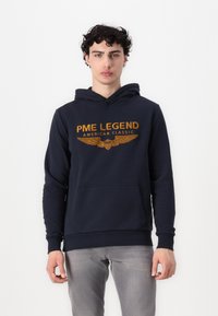 Marine-colber gemaakt van katoenmix met een voorzak. Bevat gouden tekst "PME LEGEND AMERICAN CLASSIC" en een vleugel grafisch ontwerp.