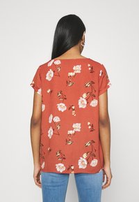 Blomstermønstret rustfarvet top med korte ærmer, flydende design og rund halsudskæring. Har lyse blomster og grønne accenter.