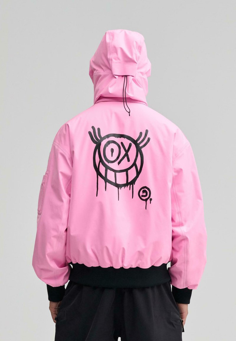 Pink bomberjakke med sort grafisk design på ryggen, med en smilende ansigt med store øjne og dryppende detaljer, ribbede manchetter og kant.