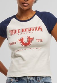 Wit en marineblauw raglan t-shirt met rode grafische tekst "TRUE RELIGION" en logo; aansluitende stijl met korte mouwen en een ronde hals.