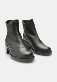 Botines de cuero negro hasta el tobillo con punta afilada, parte superior ligeramente curvada y tacón cuadrado. Textura suave sin detalles decorativos visibles.