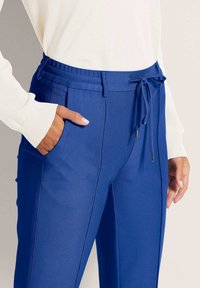 Blauwe broek met een gestructureerd ontwerp, voorzien van een koord in de taille, zijzakken en een textuurpatroon van de stof.