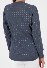 Granatowy sweter wykonany z miękkiego materiału, zdobiony białymi kropkami i małymi wzorami kotwic, z czerwonymi akcentami oraz ściągaczami przy mankietach i u dołu.