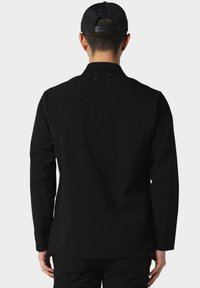 Must täiskasvitud must pikakä sleeves särk sirge lõikega, traditsioonilise kraega ja peene õmbluse detailiga seljal. Sile, ühtlane kangas.