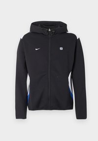 Melna kapuce ar rāvējslēdzēju jaka ar baltām un zilām sānu paneļiem, Nike logotips uz kreisā krūšu rajona un mazs taisnstūra formas emblēma uz labā krūšu rajona.