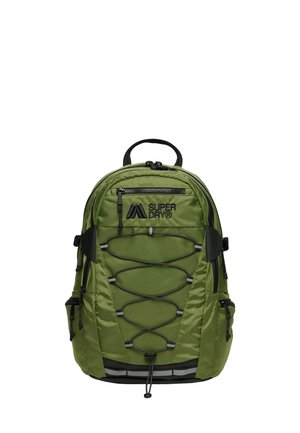 Un sac à dos vert olive avec une finition texturée, présentant des accents noirs, un cordon bungee ajustable, plusieurs zips et des poches latérales.