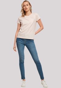 T-shirt rose clair à manches courtes associé à un jean skinny bleu et des baskets blanches. Design simple, coupe décontractée, texture lisse.