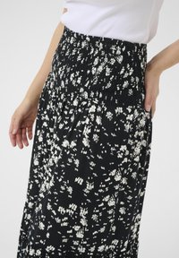 Jupe noire avec une taille smockée. Présente un motif floral blanc et une coupe fluide, fabriquée en tissu léger.