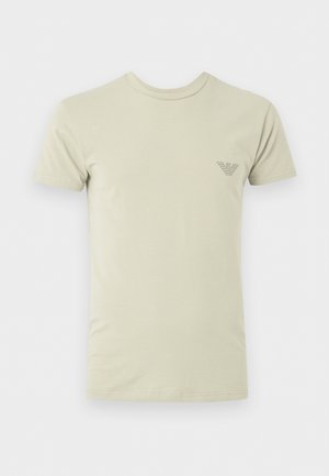 Beigenvärinen lyhythihainen t-paita, pyöreä kaulus ja vasemmalla rinnalla pieni tumma painettu logo.