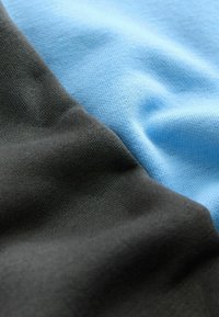 Gros plan sur un tissu doux et texturé avec des sections noires et bleu clair montrant le motif tricoté et des plis délicats.